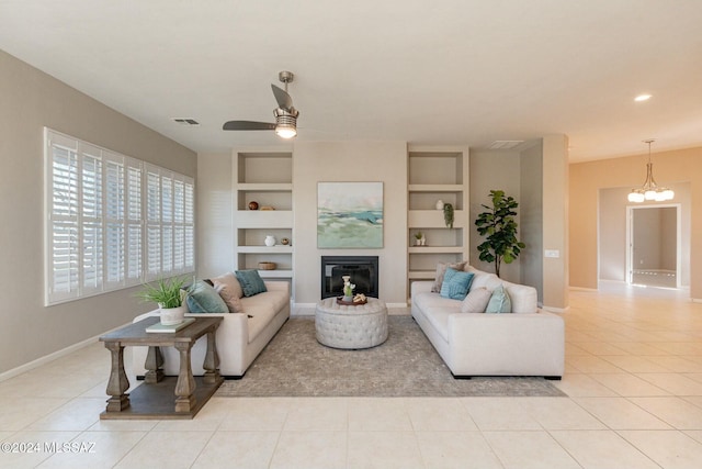 5152 W Heritage Gateway Pl, Marana, AZ 85658 - living room featuring ceiling fan with notable chandelier, a glass covered fireplace, light tile patterned floors, built in features, and baseboards