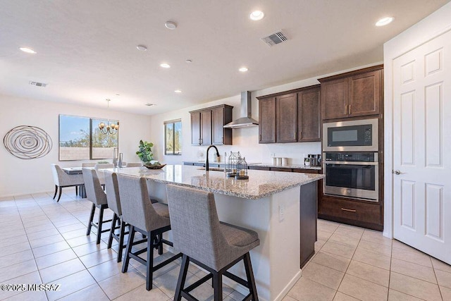 10965 N Cormac Ave, Tucson, AZ 85742 - kitchen featuring stainless steel oven, wall chimney range hood, built in microwave, an island with sink, and a kitchen breakfast bar