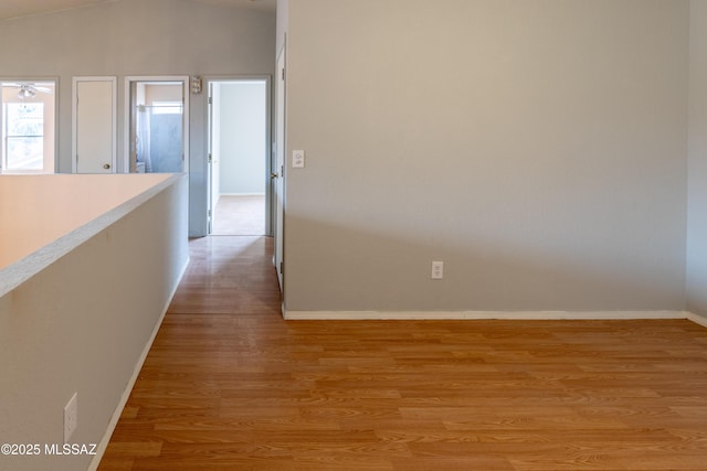 hall featuring baseboards, lofted ceiling, and light wood-type flooring