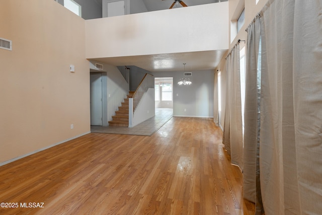 entrance foyer featuring light wood-style flooring, visible vents, a chandelier, a high ceiling, and stairs