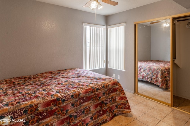 bedroom featuring a textured wall, a ceiling fan, light tile patterned floors, a closet, and baseboards
