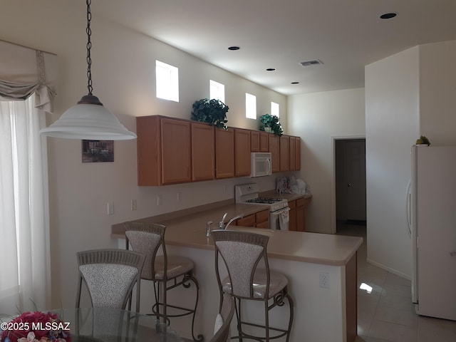 kitchen with brown cabinetry, white appliances, a breakfast bar area, light countertops, and a peninsula