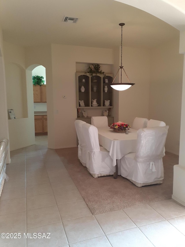 dining space featuring arched walkways, visible vents, and light tile patterned floors