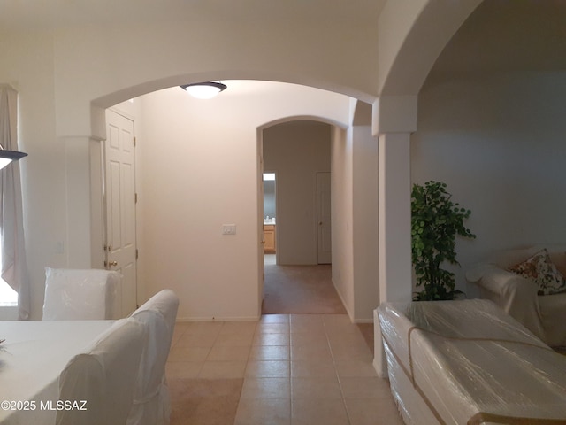 hallway with arched walkways, baseboards, light carpet, and light tile patterned floors