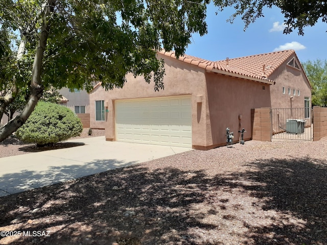 view of side of property with fence, stucco siding, a tile roof, driveway, and a garage
