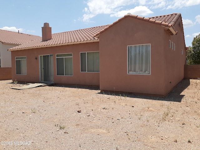 rear view of property with a chimney, a tiled roof, and stucco siding
