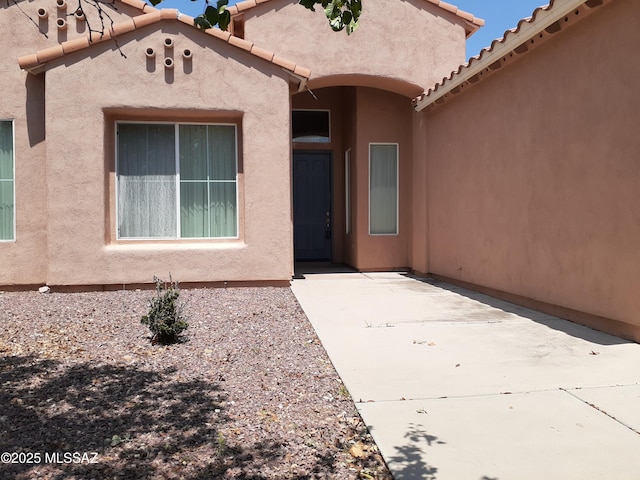entrance to property with a patio area, a tiled roof, and stucco siding