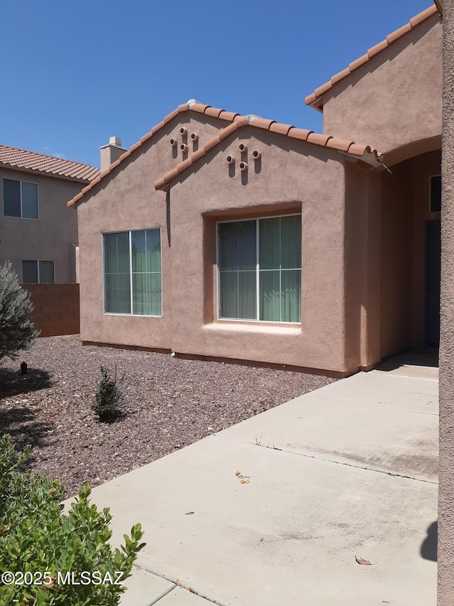 exterior space with stucco siding, a tile roof, a chimney, and fence
