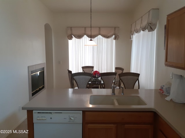 kitchen with light countertops, dishwasher, a sink, arched walkways, and a peninsula