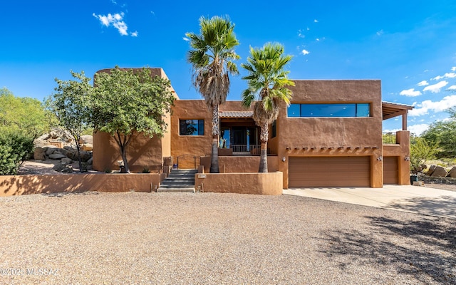 pueblo-style home with stucco siding, driveway, a balcony, and a garage