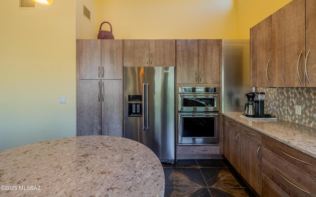kitchen featuring brown cabinetry, visible vents, tasteful backsplash, light stone countertops, and stainless steel appliances