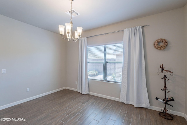 spare room featuring wood finished floors, a chandelier, visible vents, and baseboards