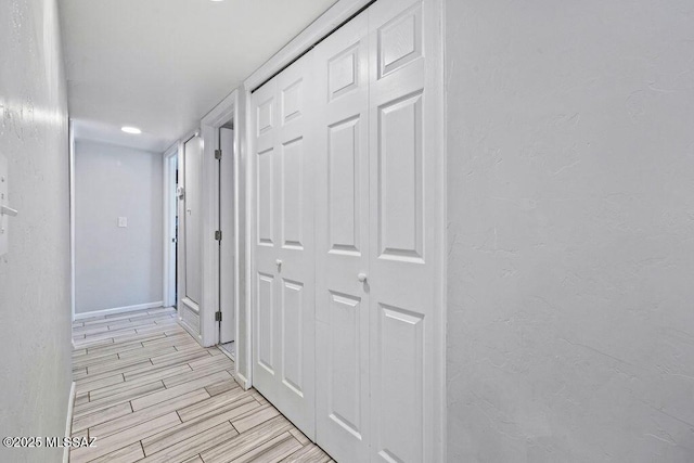 corridor with baseboards, wood tiled floor, and a textured wall