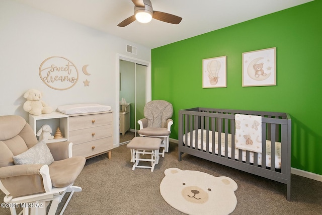 carpeted bedroom with ceiling fan, visible vents, a crib, baseboards, and a closet