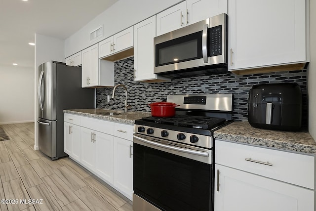 kitchen featuring backsplash, stainless steel appliances, white cabinets, and visible vents