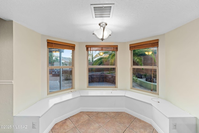 unfurnished dining area with light tile patterned floors, a textured ceiling, and visible vents