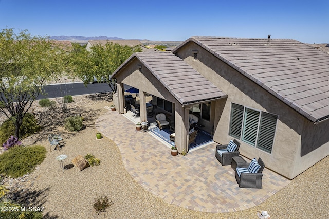 rear view of property with stucco siding, a tiled roof, and a patio