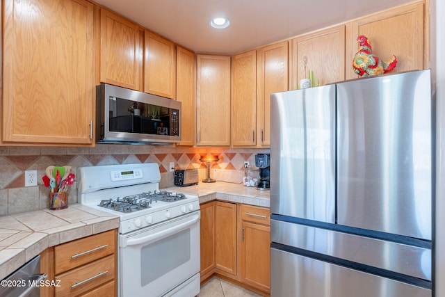 kitchen featuring recessed lighting, light tile patterned floors, appliances with stainless steel finishes, backsplash, and tile countertops