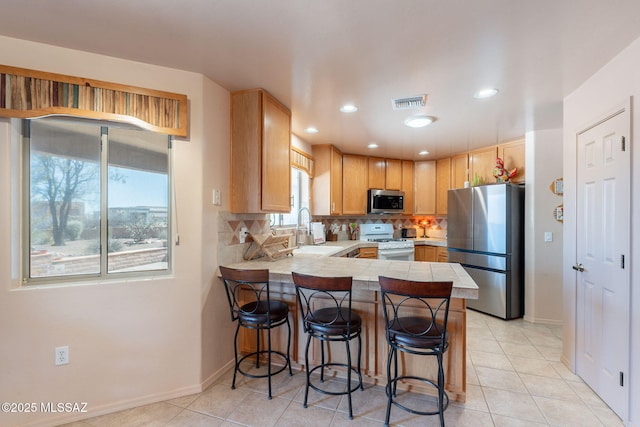 kitchen with a sink, a kitchen breakfast bar, visible vents, a peninsula, and appliances with stainless steel finishes