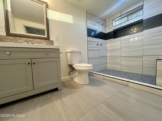 full bath featuring toilet, tiled shower, vanity, and baseboards