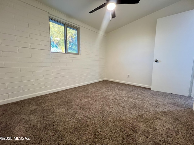 carpeted empty room with ceiling fan, brick wall, and baseboards