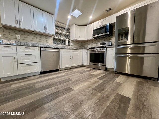 kitchen with light wood finished floors, backsplash, light stone counters, white cabinetry, and appliances with stainless steel finishes