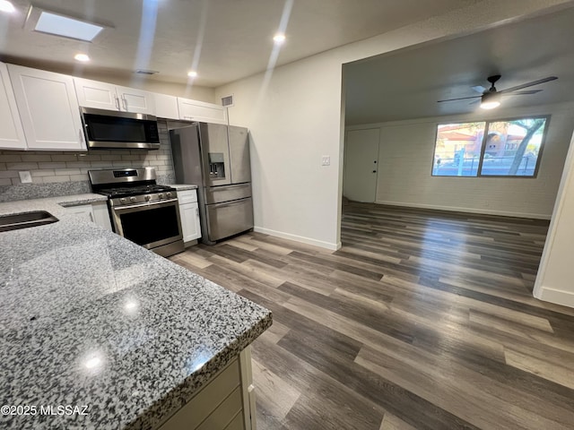 kitchen with light stone countertops, stainless steel appliances, tasteful backsplash, white cabinetry, and wood finished floors