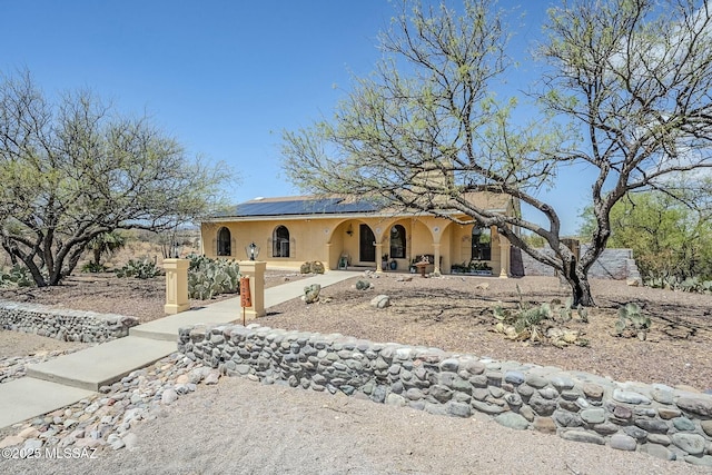 view of front of home featuring solar panels, stucco siding, and covered porch