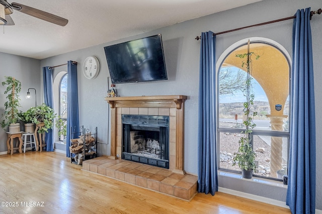 living room featuring a textured ceiling, baseboards, a fireplace, wood finished floors, and a ceiling fan