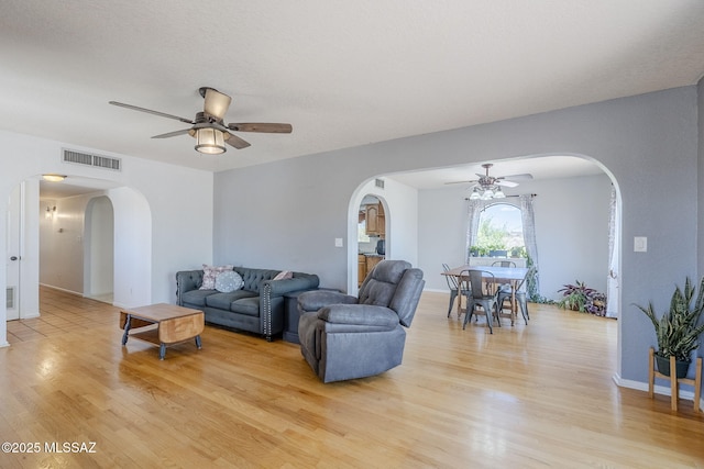 living area featuring ceiling fan, visible vents, baseboards, arched walkways, and light wood-type flooring
