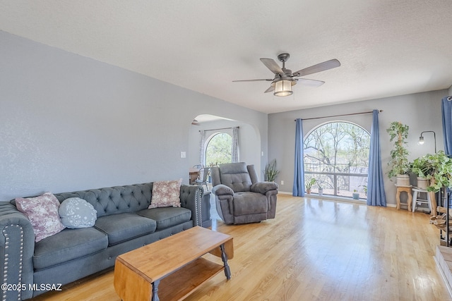 living area featuring baseboards, light wood-type flooring, arched walkways, and a ceiling fan