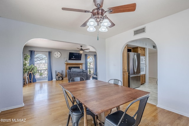dining area with visible vents, arched walkways, ceiling fan, and a fireplace