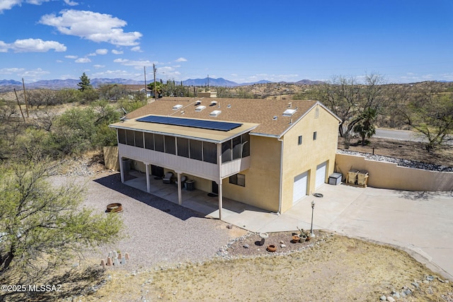 exterior space featuring a sunroom, a mountain view, roof mounted solar panels, concrete driveway, and an attached garage