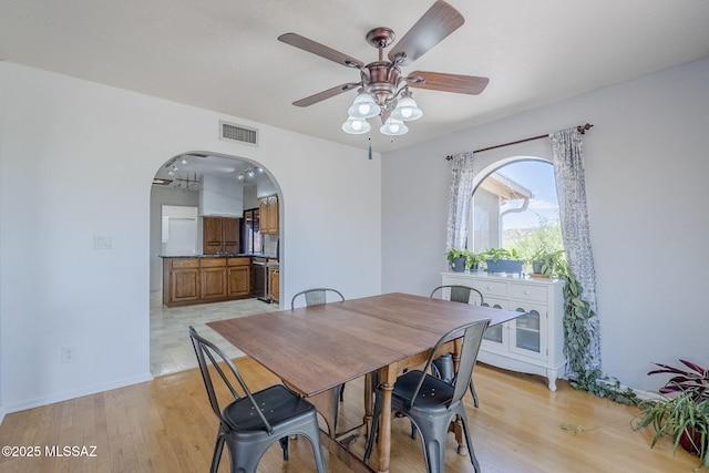 dining area featuring visible vents, arched walkways, ceiling fan, and light wood-style flooring