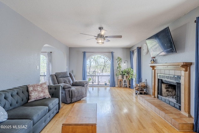 living room featuring a fireplace, wood finished floors, a ceiling fan, and arched walkways