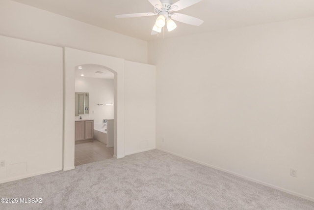 unfurnished bedroom featuring baseboards, arched walkways, and light colored carpet