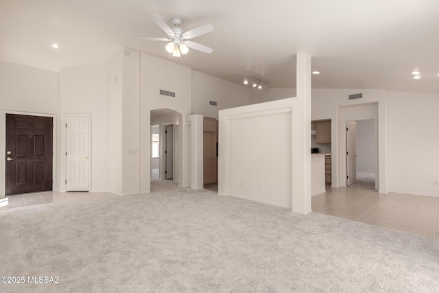 unfurnished living room with visible vents, ceiling fan, arched walkways, light tile patterned flooring, and light carpet
