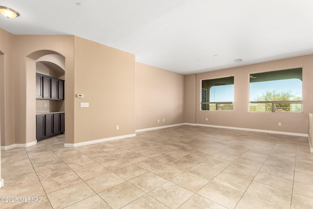 spare room featuring light tile patterned floors, arched walkways, and baseboards