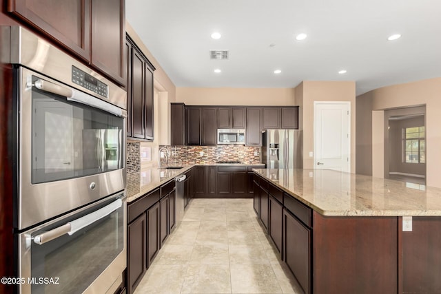 kitchen featuring appliances with stainless steel finishes, a sink, visible vents, tasteful backsplash, and a spacious island