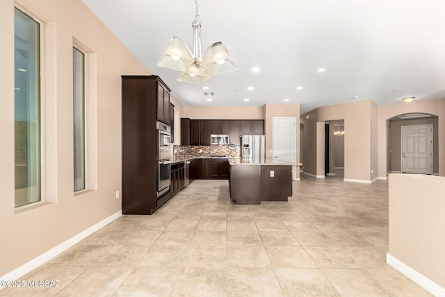 kitchen with appliances with stainless steel finishes, arched walkways, dark brown cabinets, light countertops, and a notable chandelier