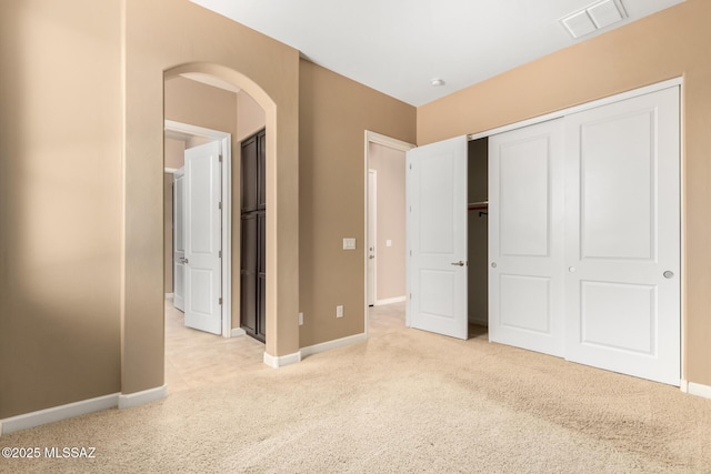 unfurnished bedroom featuring light colored carpet, visible vents, arched walkways, baseboards, and a closet