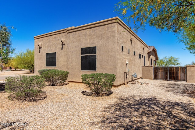 view of side of home featuring fence, a gate, and stucco siding