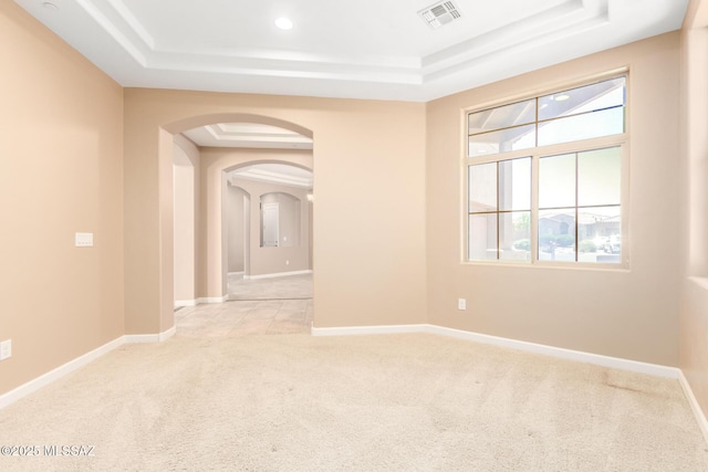 empty room featuring visible vents, arched walkways, a raised ceiling, and light carpet