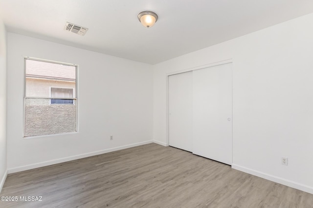 unfurnished bedroom with baseboards, visible vents, wood finished floors, and a closet