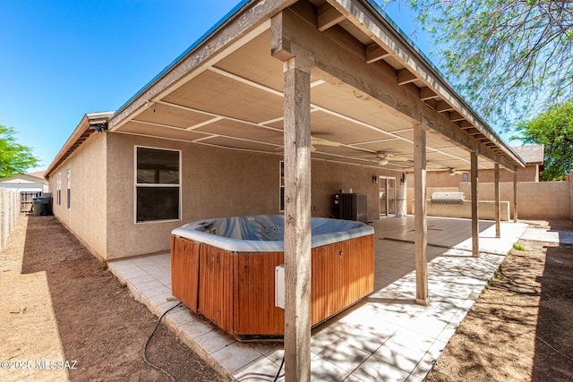 exterior space featuring a patio, central AC unit, a fenced backyard, a hot tub, and stucco siding