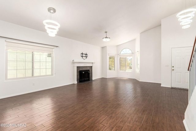 unfurnished living room with dark wood-style flooring, baseboards, a chandelier, and a tiled fireplace