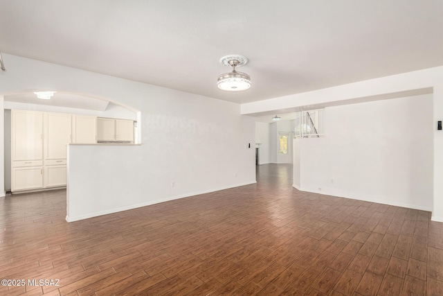unfurnished room featuring baseboards, dark wood-style flooring, and arched walkways