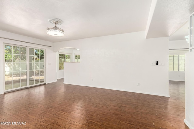 empty room featuring baseboards, arched walkways, and wood finished floors