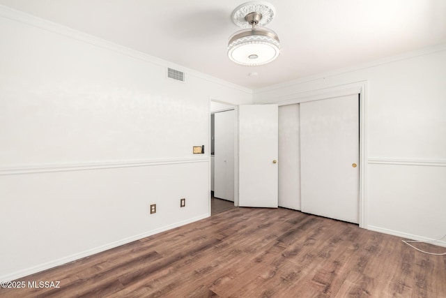 unfurnished bedroom featuring visible vents, ornamental molding, wood finished floors, and a closet