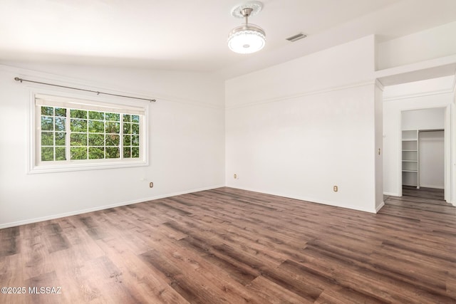 unfurnished room with visible vents, baseboards, dark wood-style floors, and vaulted ceiling